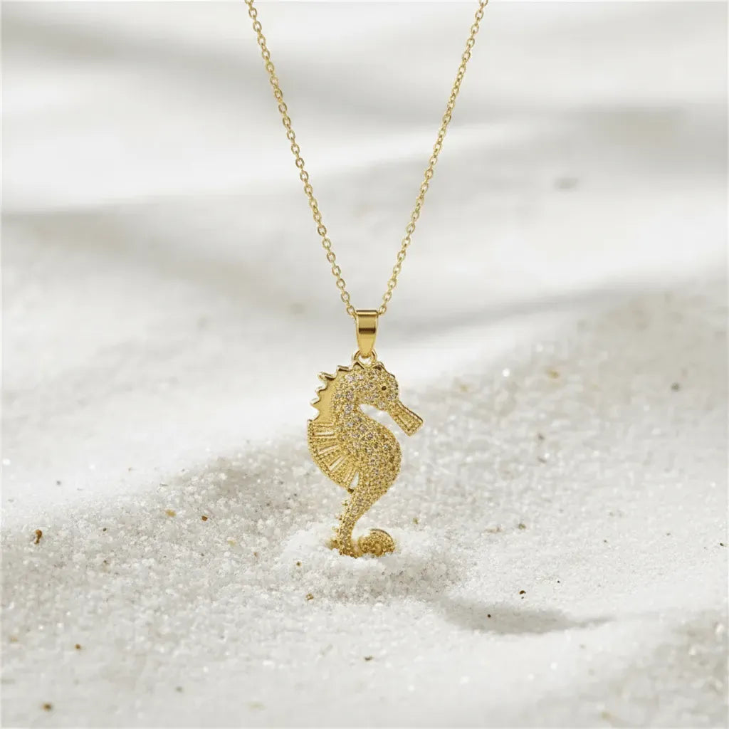 Gold seahorse necklace on a sandy background