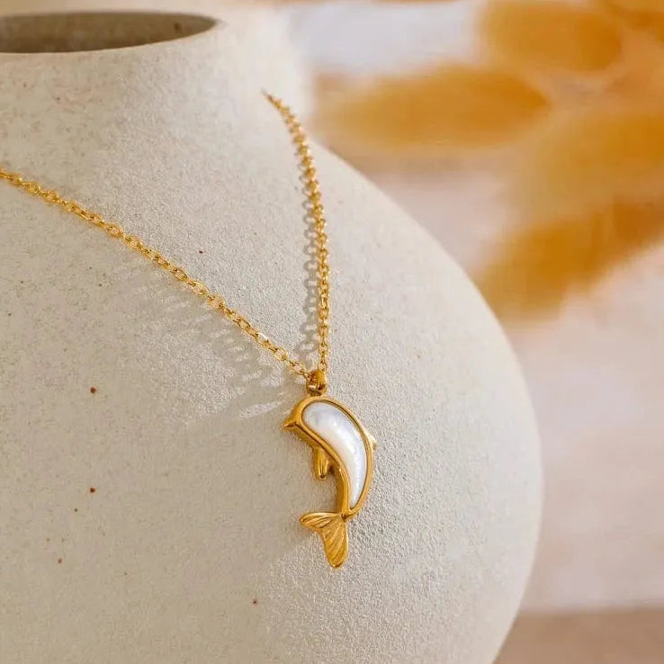 Gold necklace with a dolphin pendant on a textured surface