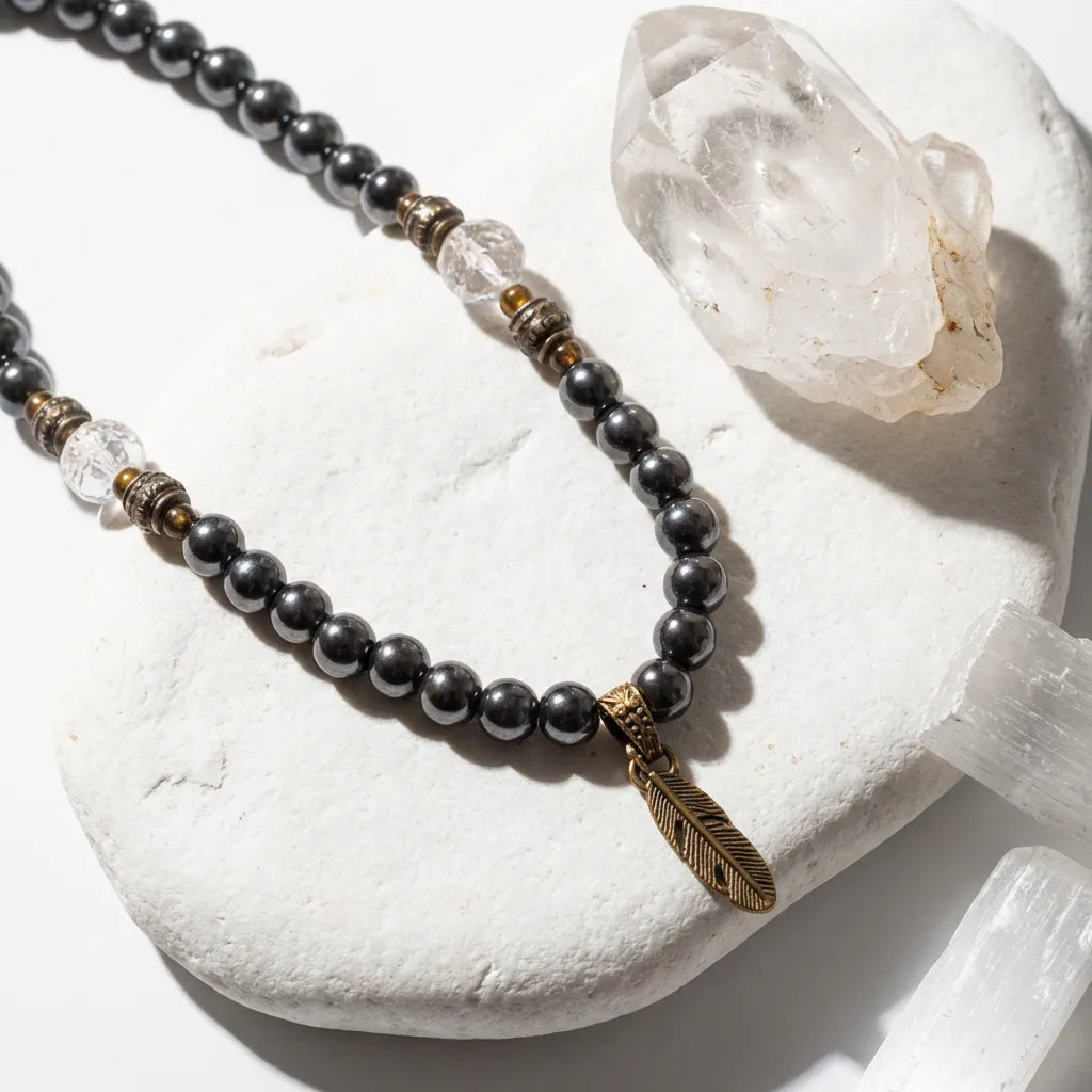 Necklace with black beads and a feather charm on a white stone surface