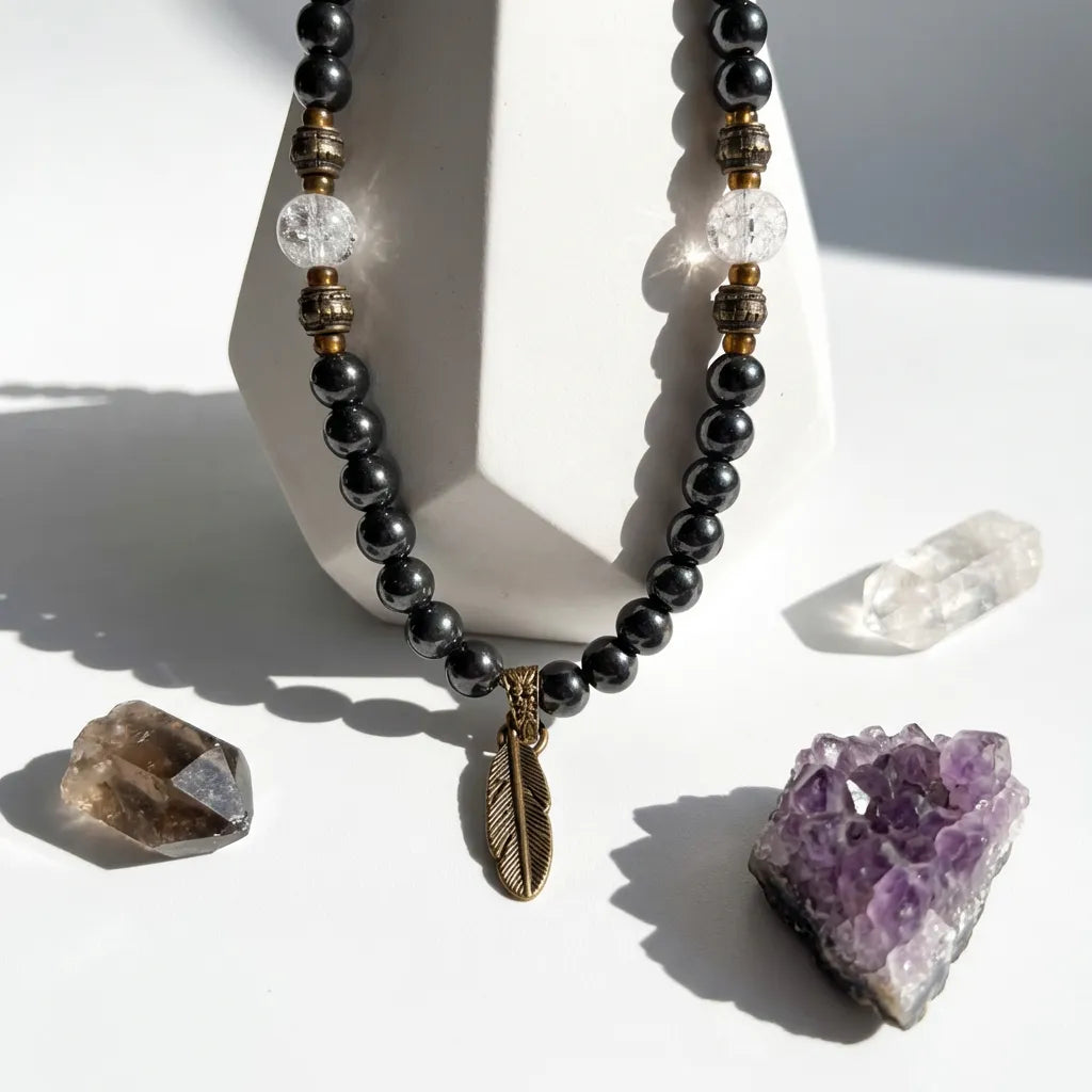 Necklace with black beads and a feather pendant on a white surface with crystals.