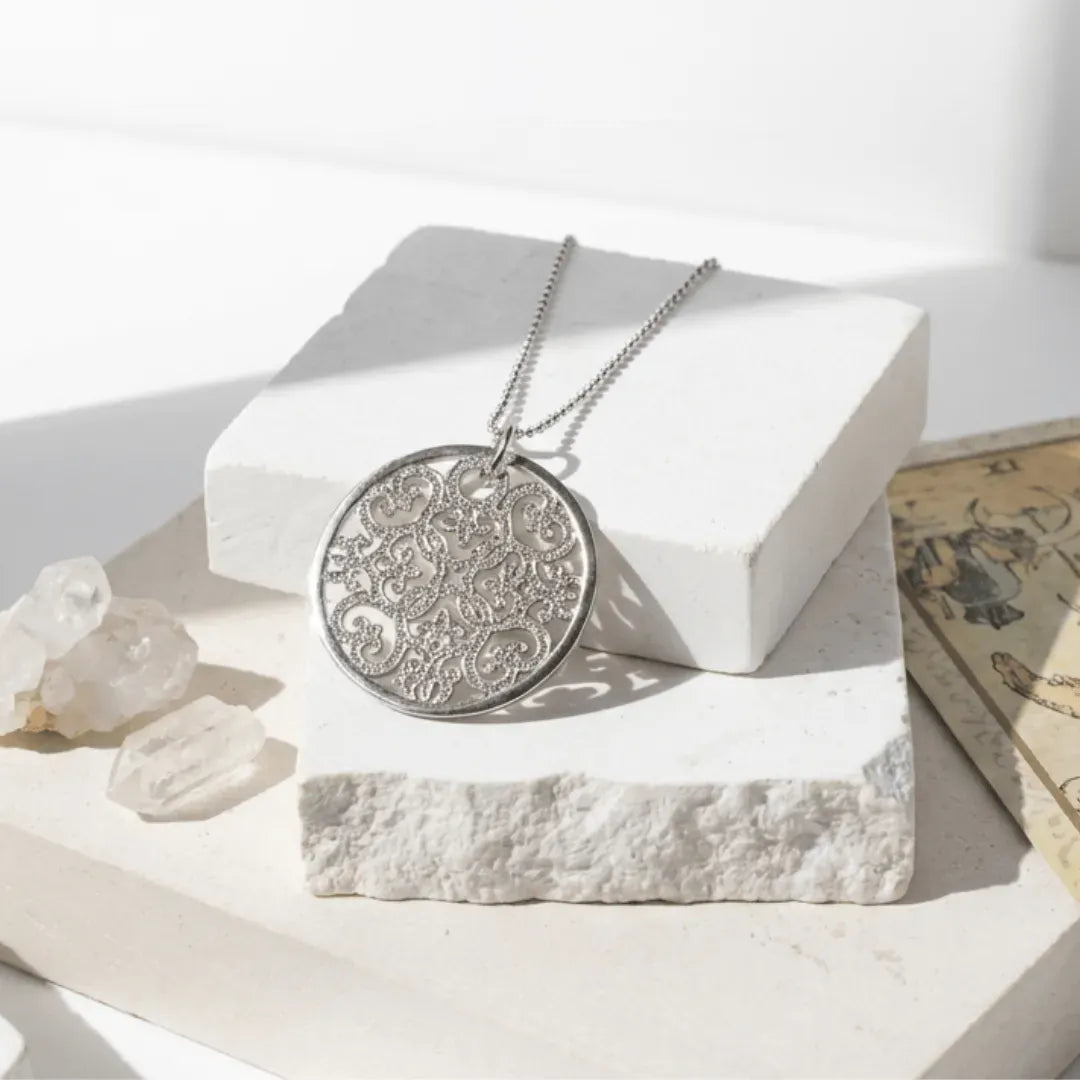 Silver necklace with a detailed pendant on a white surface