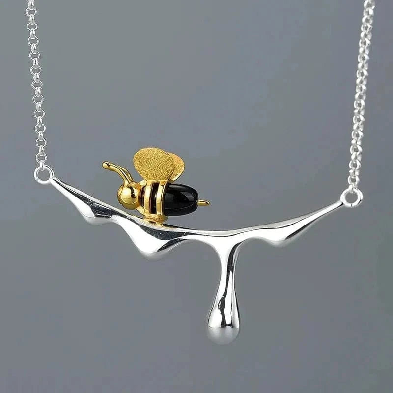 Necklace with a gold bee and black body pendant on a silver chain against a gray background