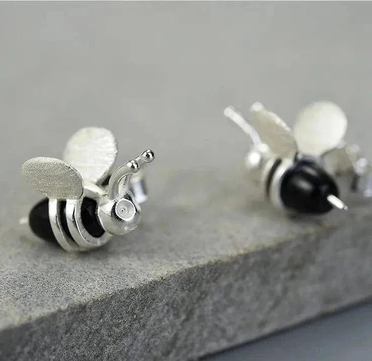 Silver bee-shaped earrings on a stone surface