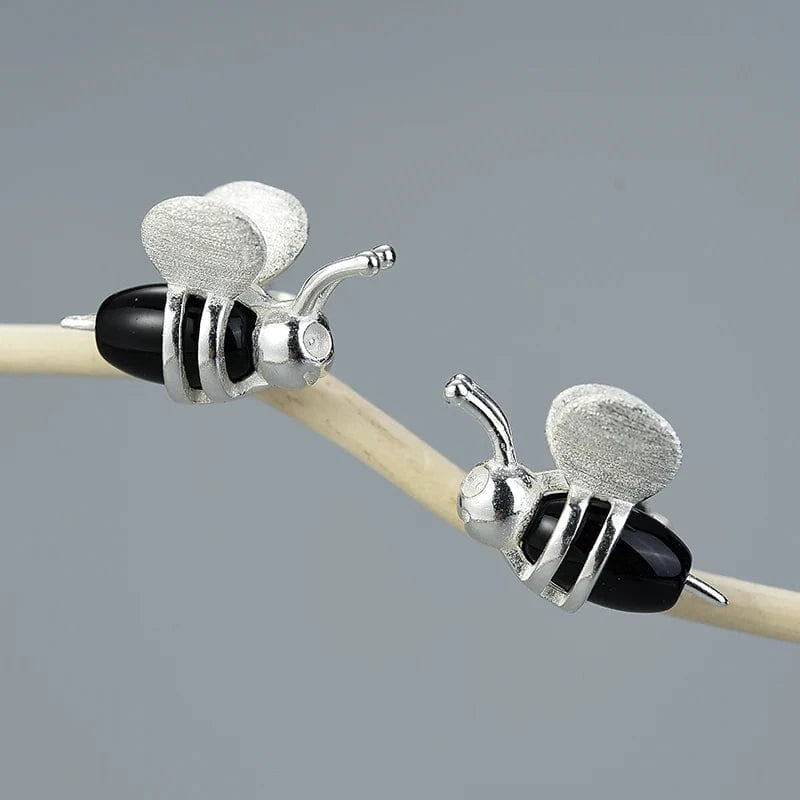 Silver bee-shaped earrings with black accents on a gray background