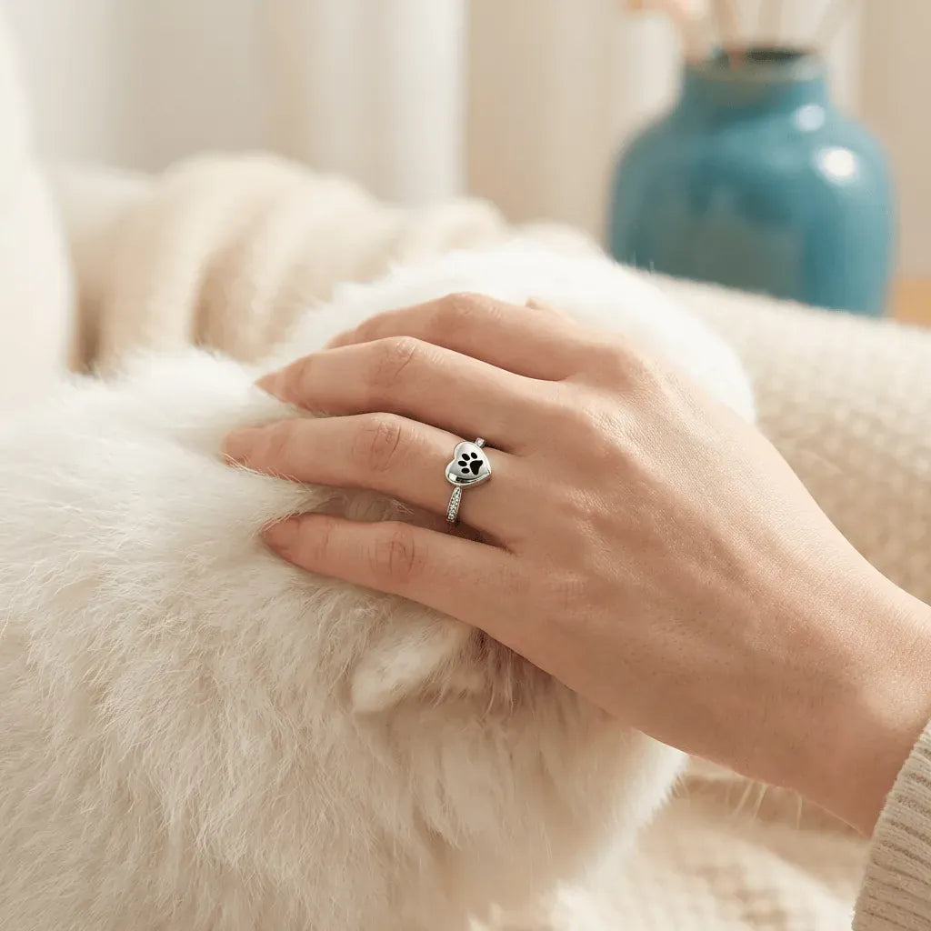 Hand wearing a silver ring with a paw print design, petting a fluffy white animal.
