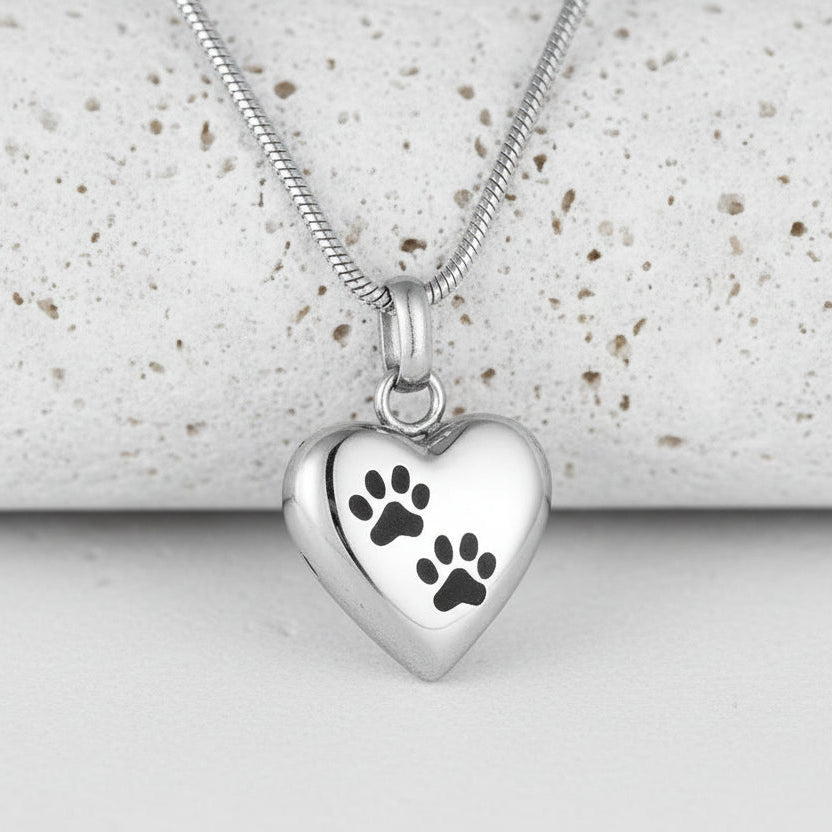 Silver heart-shaped pendant with paw prints on a white background