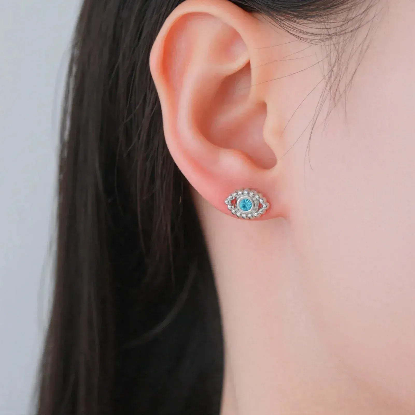 Close-up of an ear wearing a decorative earring with a blue gemstone on a plain background.