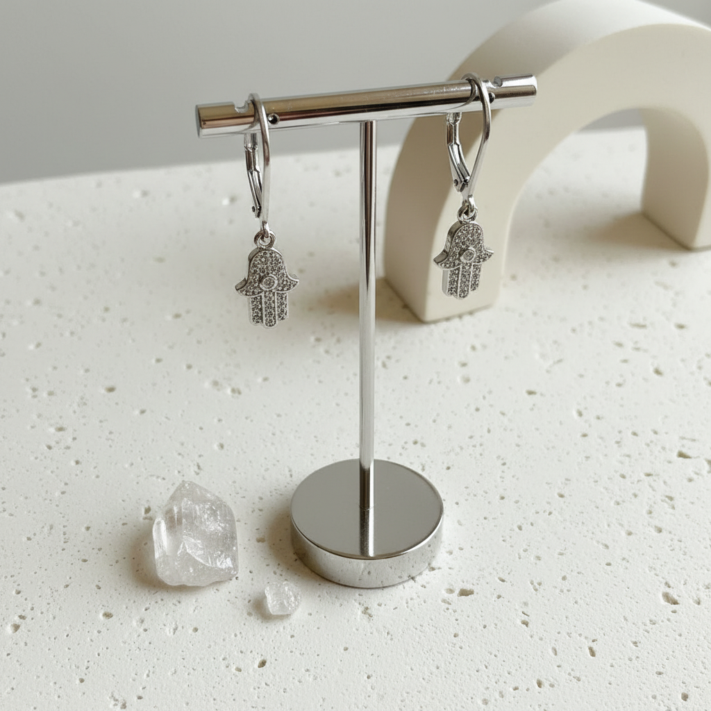 Silver plated crystal hamsa hand earrings hanging from a jewellery stand