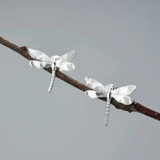Silver dragonfly earrings on a branch with a gray background