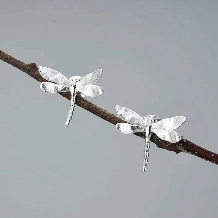 Silver dragonfly earrings on a branch with a gray background