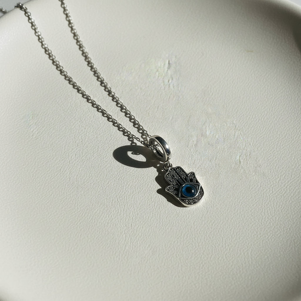 Sterling silver hamsa hand pendant with a blue evil eye centre, hanging against a plain background