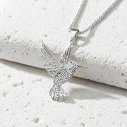 Silver hummingbird pendant on a chain against a light stone background
