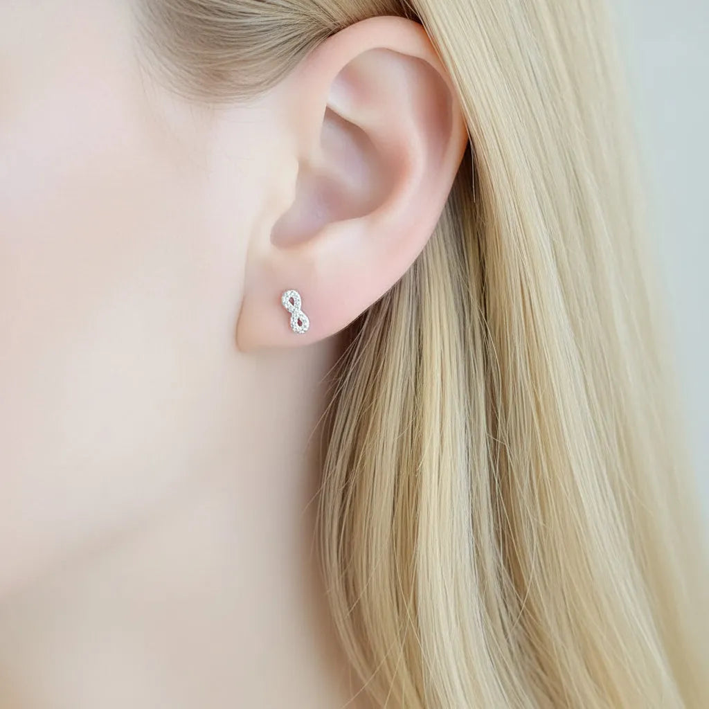 Close-up of an ear wearing a silver infinity symbol earring with dark hair.