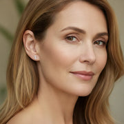 Close-up of a woman with long blonde hair wearing earrings against a neutral background