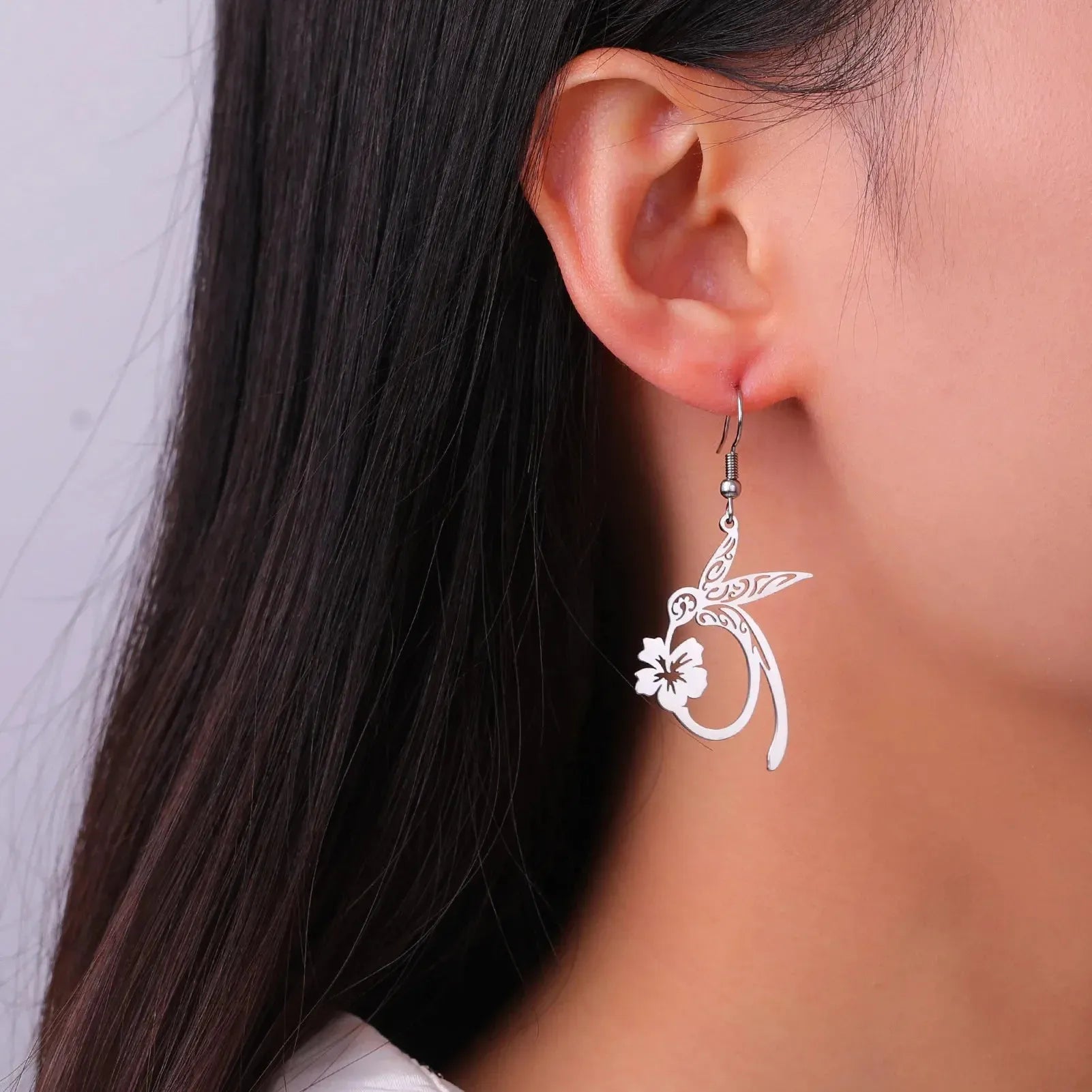 Silver earring with floral design worn by a person against a neutral background