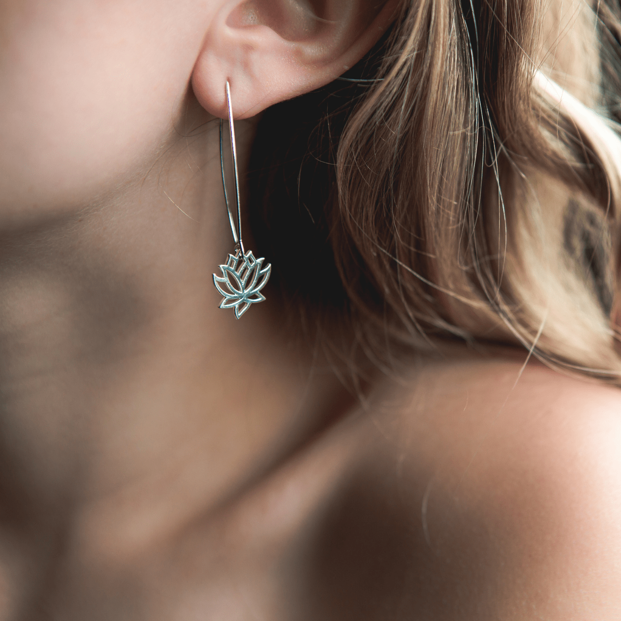 Close-up of a person wearing a silver lotus flower earring.