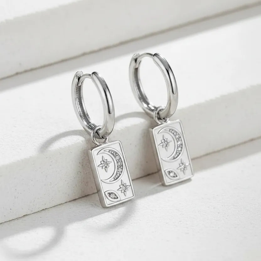 Silver hoop earrings with card-shaped charms on a light wooden surface