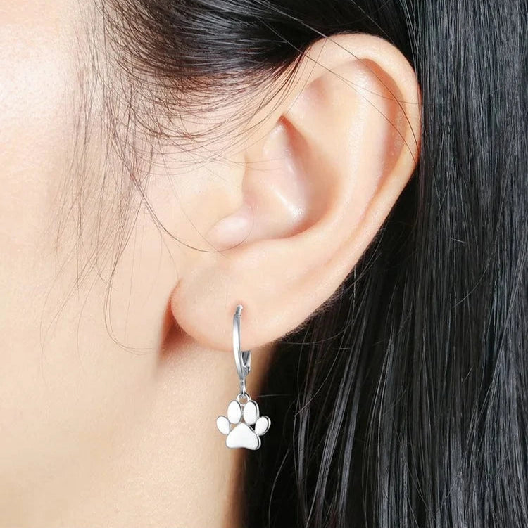 Silver hoop earrings with paw print charms worn by a person with dark hair.