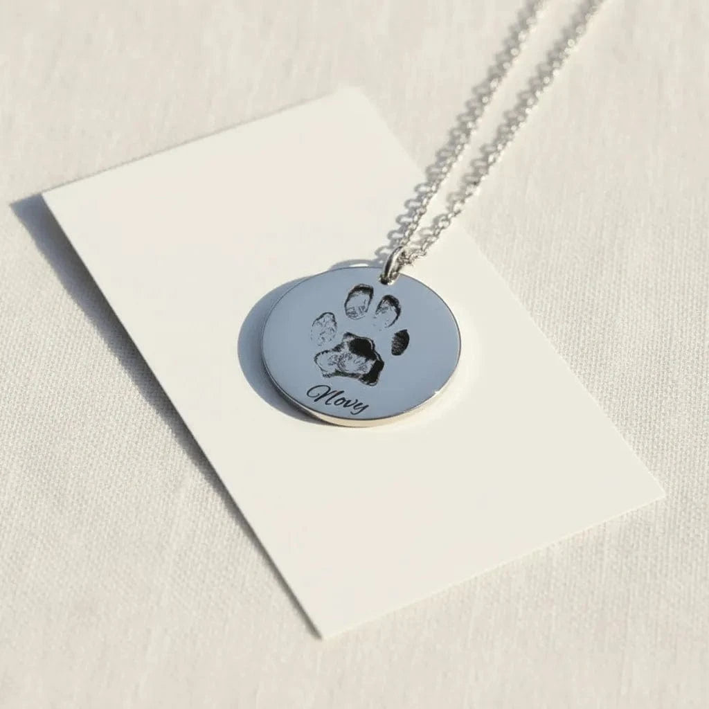 Necklace with a round pendant featuring a paw print and engraved text on a white card.