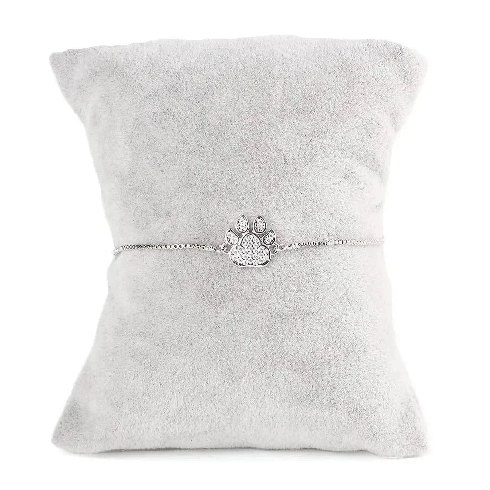 Silver bracelet with paw print charm on a gray cushion