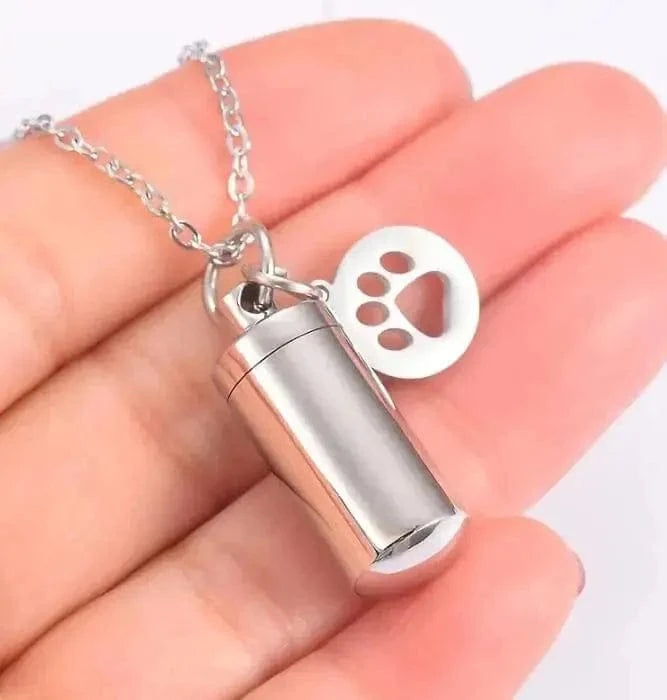 Silver cylindrical pendant with paw print charm on a chain held in hand
