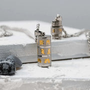 Silver cylindrical pendant with gold text and designs on a gray surface