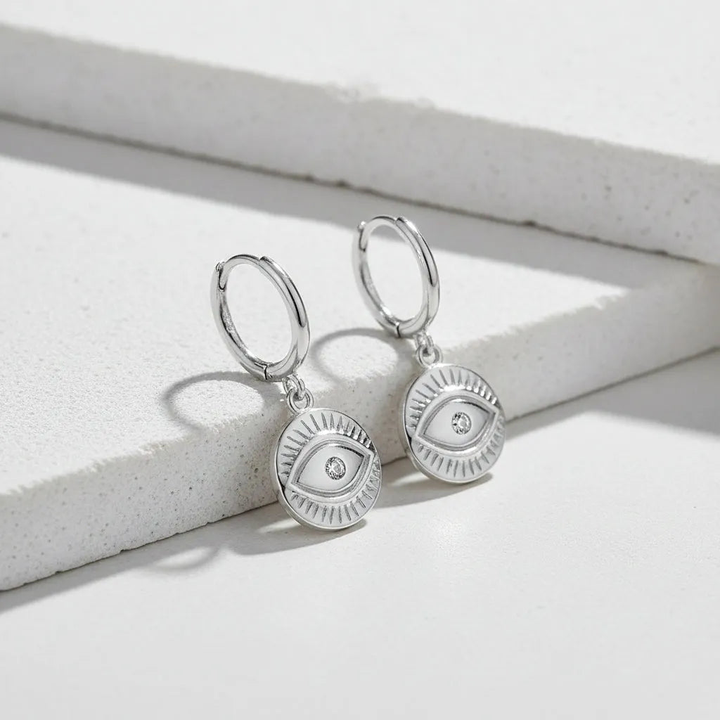 Silver earrings with eye design on a white background .