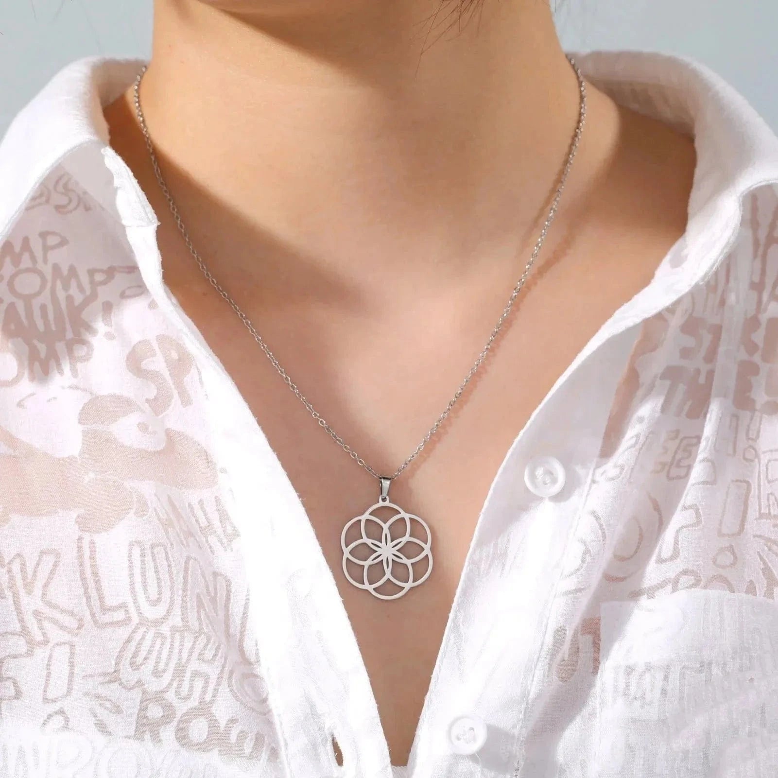 Silver necklace with a floral pendant worn by a person in a white shirt.
