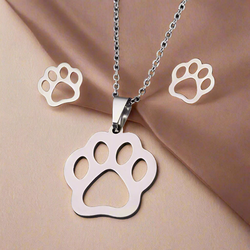 Silver paw print necklace and earrings on a beige fabric background