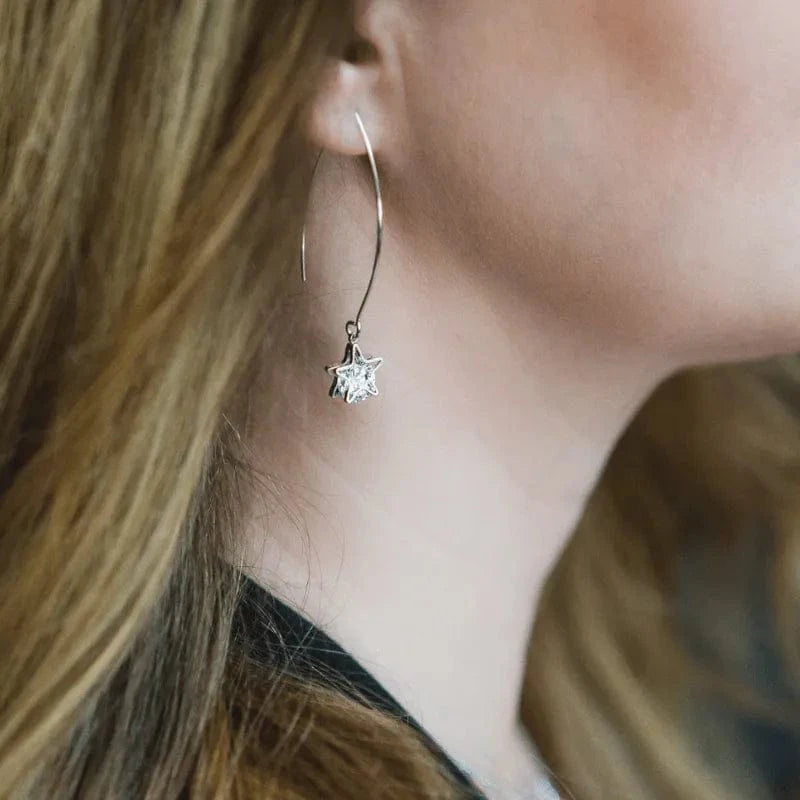 Close-up of a person wearing a silver hoop earring with a star-shaped pendant.