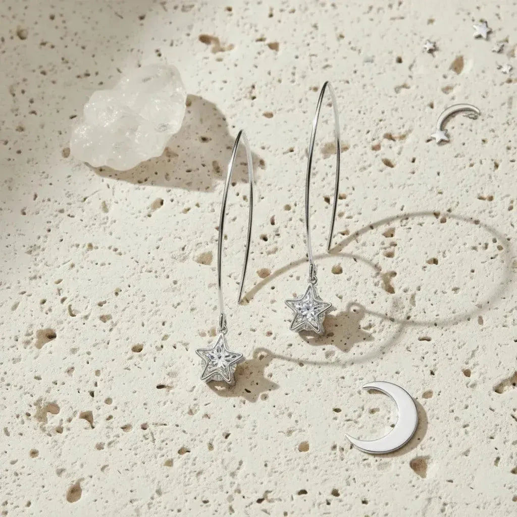 Silver earrings with star and moon designs on a textured beige surface