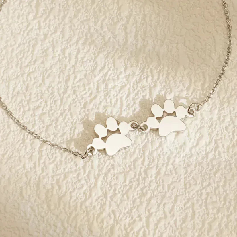 Silver necklace with paw print charms on a textured beige background