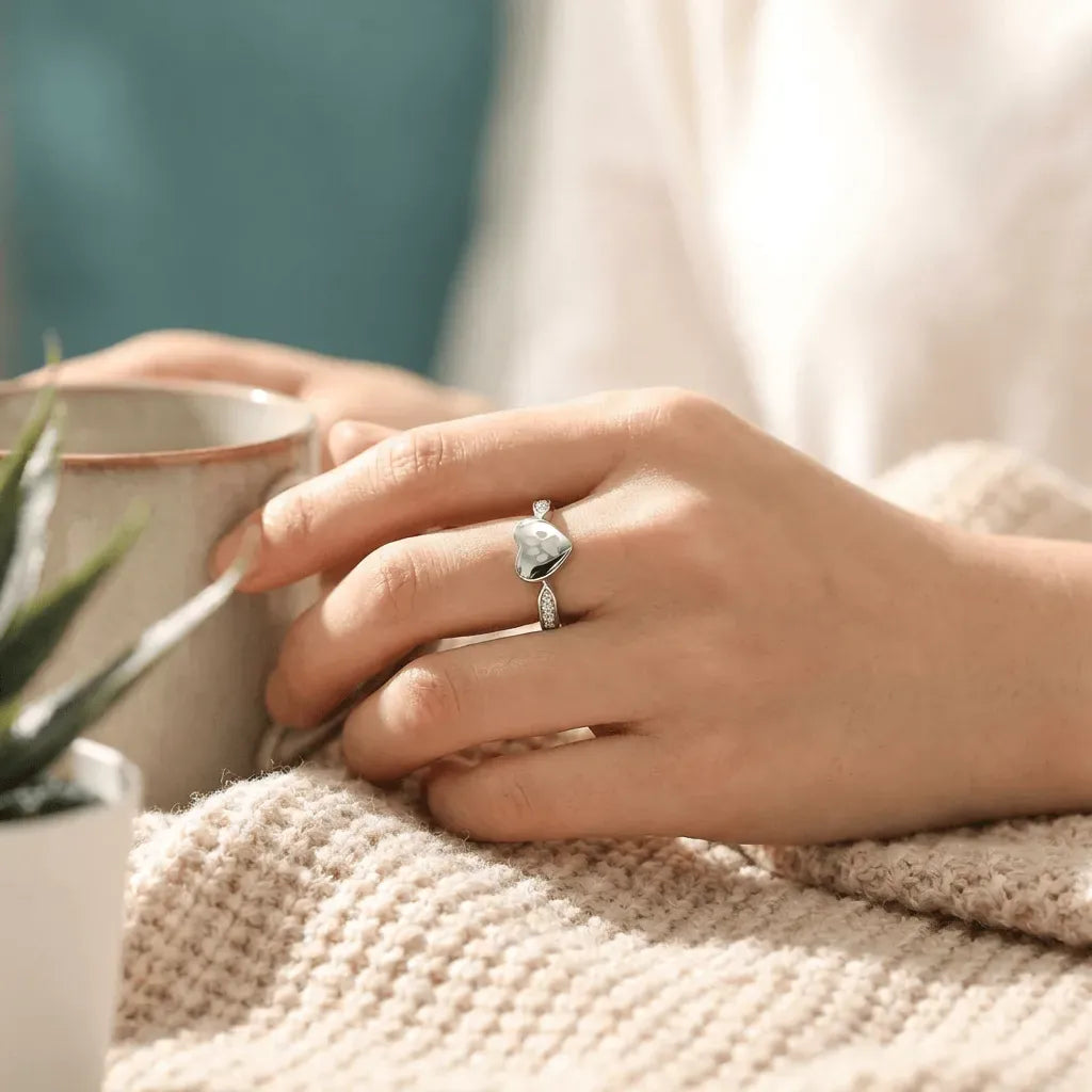 Person holding a mug with a decorative ring on a soft surface