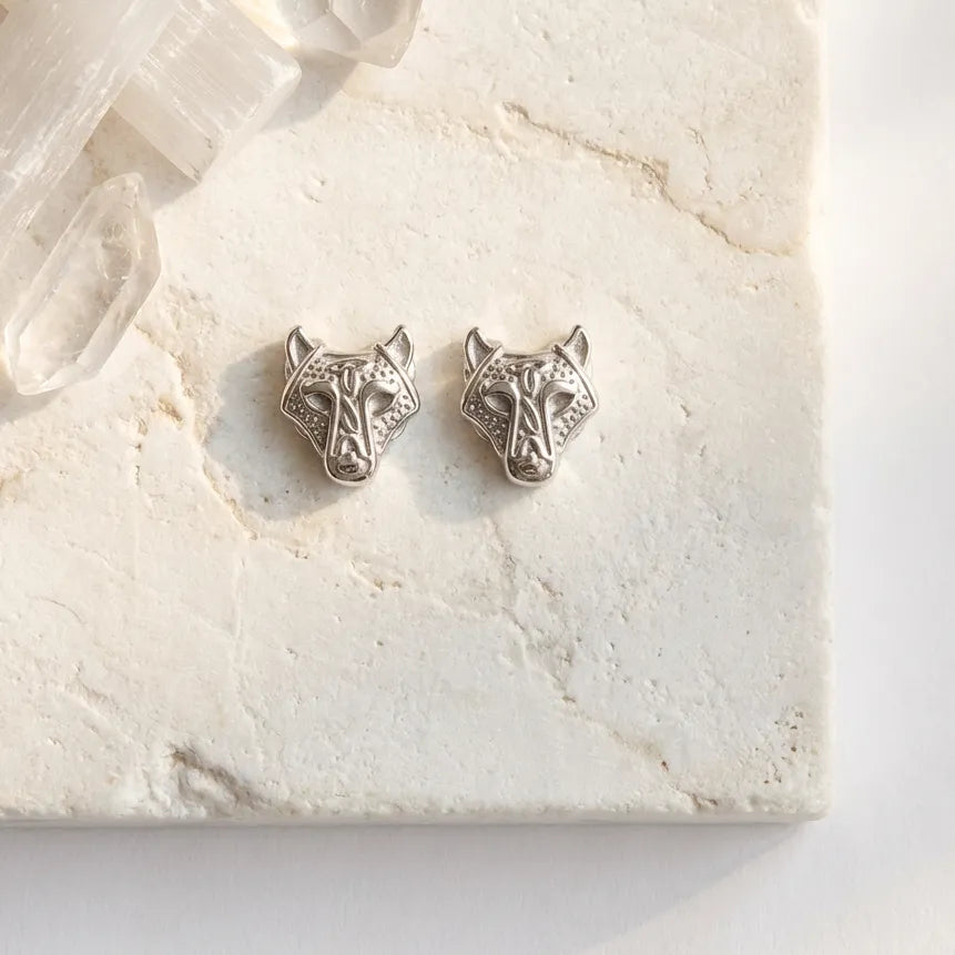 Silver wolf head stud earrings on marble — spirit animal jewelry for courage and instinct