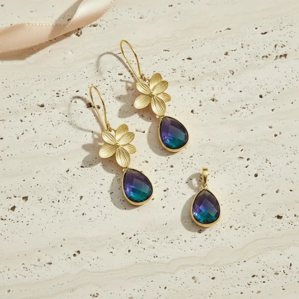 Gold earrings with floral designs and blue teardrop stones on a textured surface