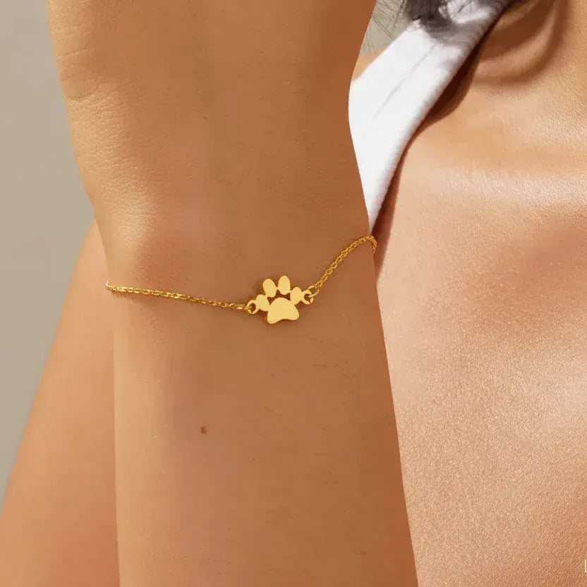 Gold bracelet with paw print design on a person's wrist against a neutral background