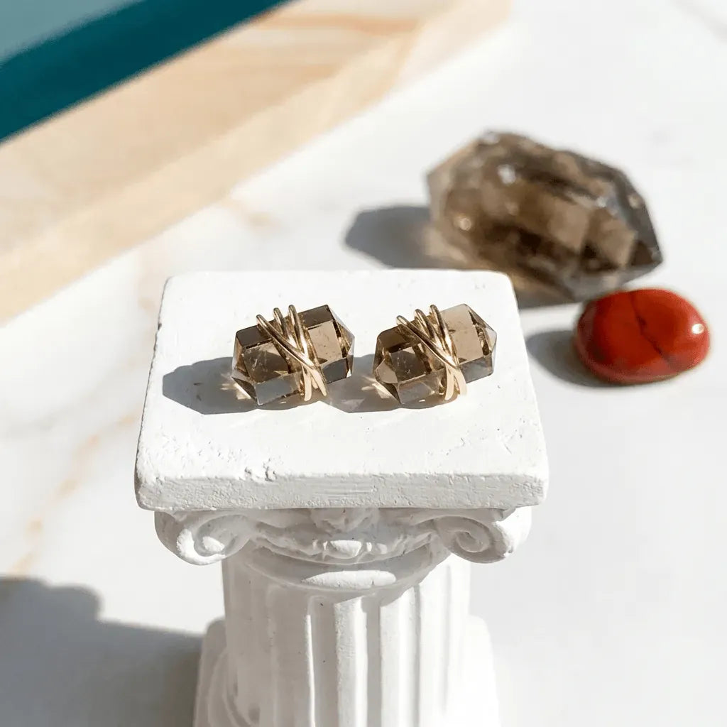 Gold geometric earrings on a white pedestal with a natural stone background