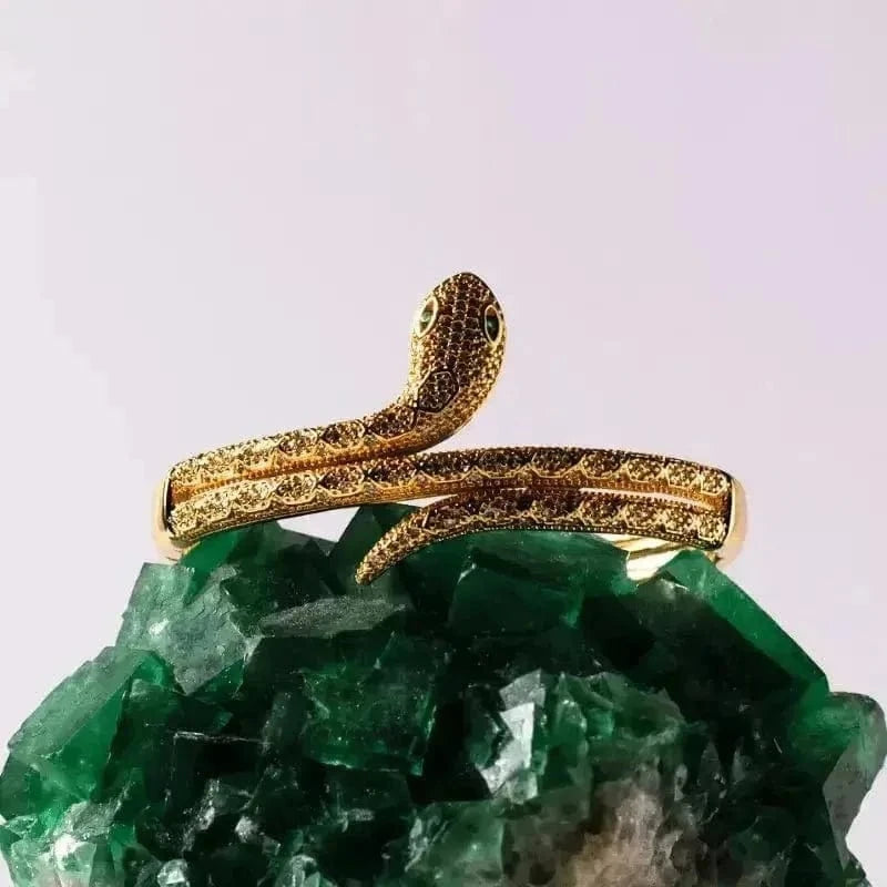 Gold snake-shaped ring on a green crystal with a light purple background