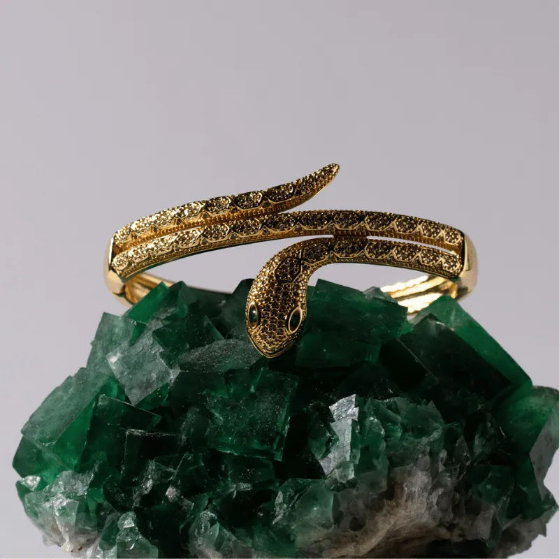 Gold snake-shaped bracelet on a green crystal background
