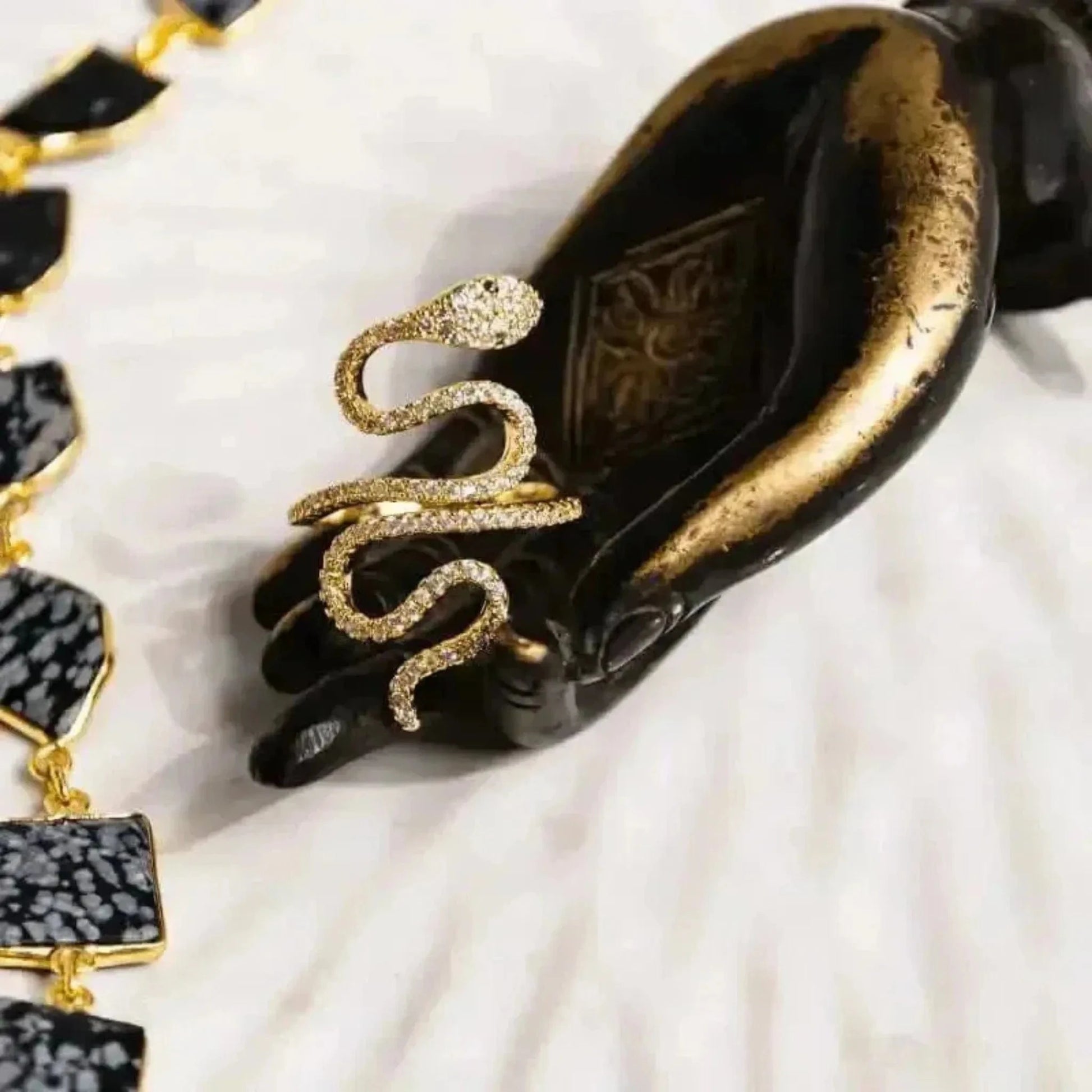 A gold-plated snake ring with crystal embellishments displayed on a black figure's hand.