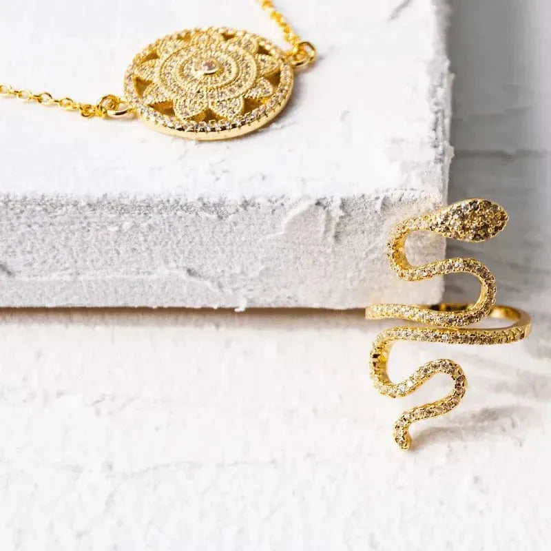 Gold necklace and snake-shaped bracelet on a textured white surface