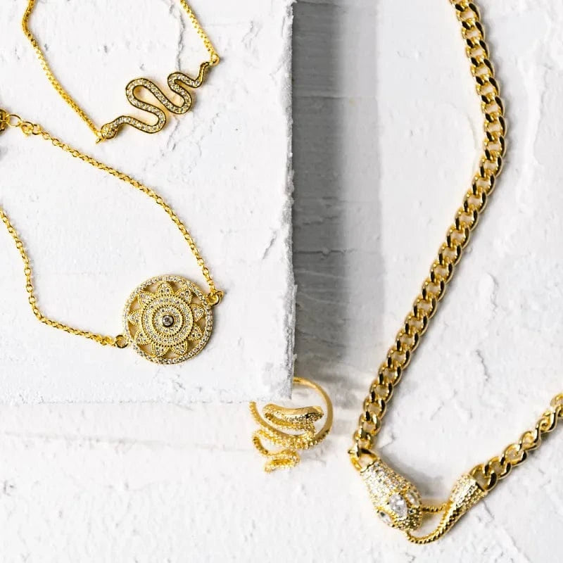 Gold jewelry including necklaces and a ring on a textured white surface