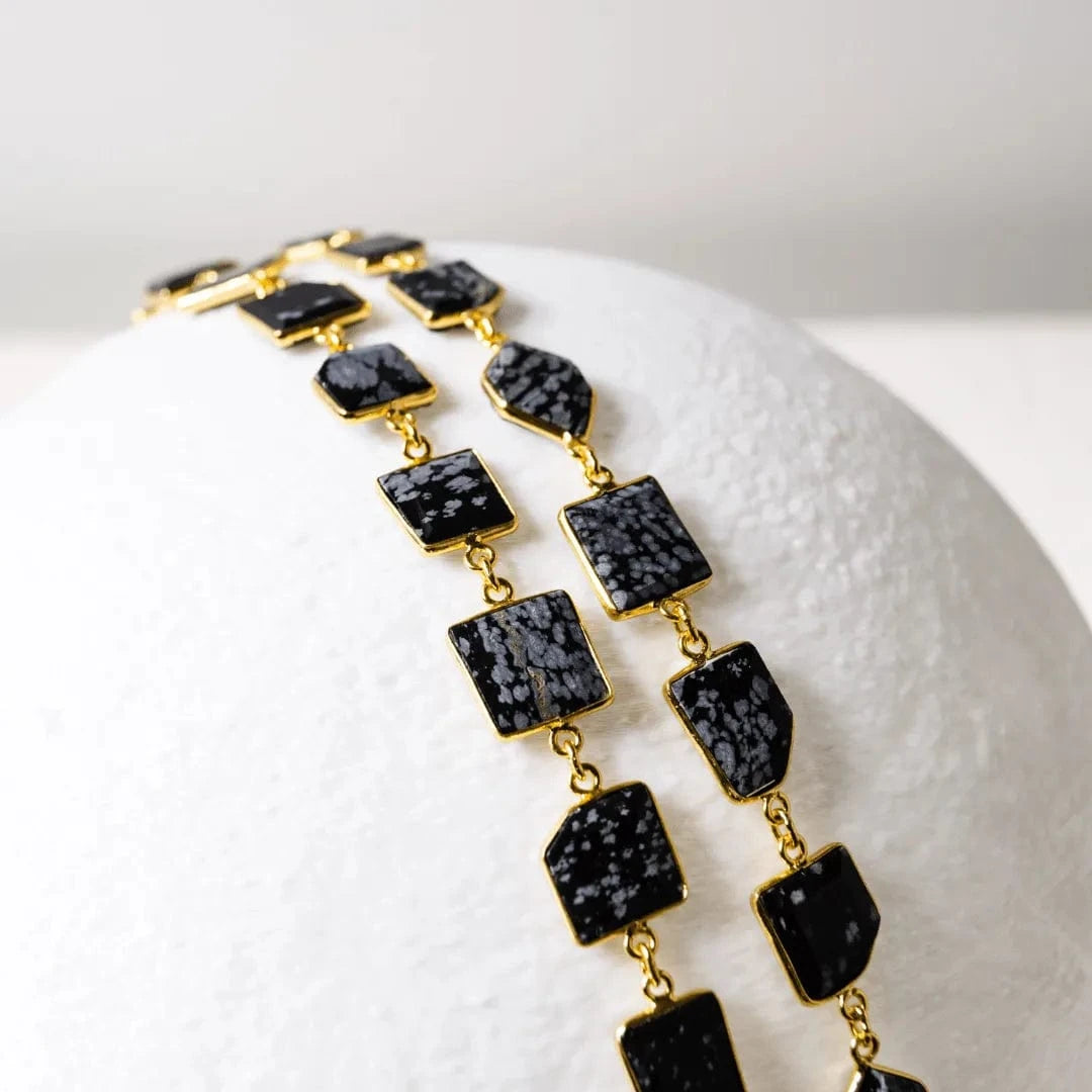 Gold necklace with black square stones on a white background