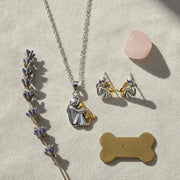 Jewelry set with necklace, earrings, and dog tag on a textured surface with lavender and pink stone.