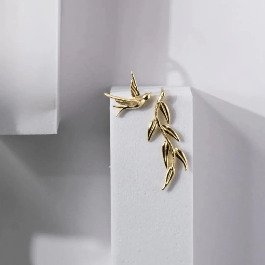 Gold bird and branch earrings on a white stand with a light gray background