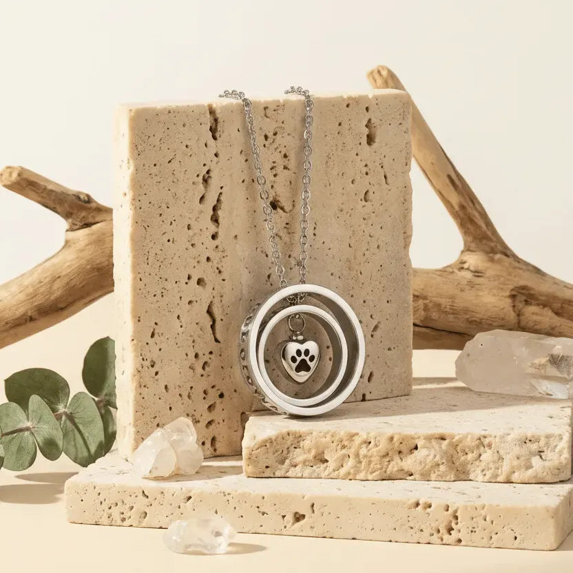 Necklace with a paw print pendant on a natural stone stand with driftwood and eucalyptus leaves in the background.