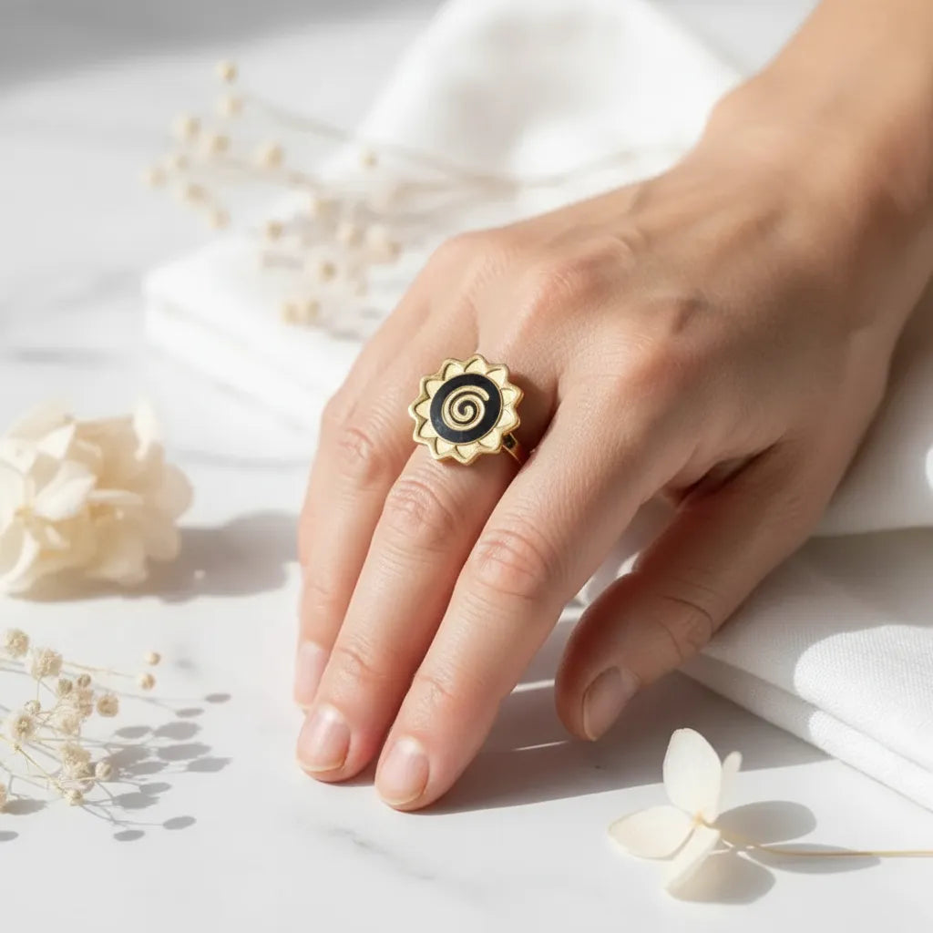 Hand wearing a gold and black spiral ring on a light background with flowers.