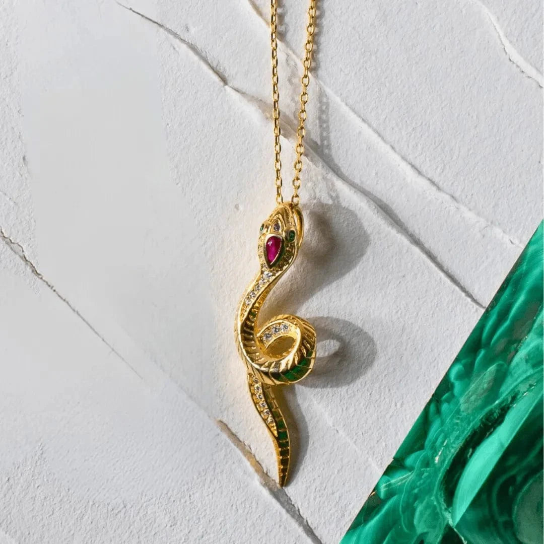 Gold snake-shaped necklace with gemstones on a light marble background