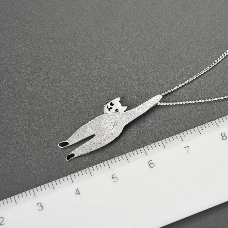 Silver cat-shaped pendant on a chain with a ruler for scale on a gray background