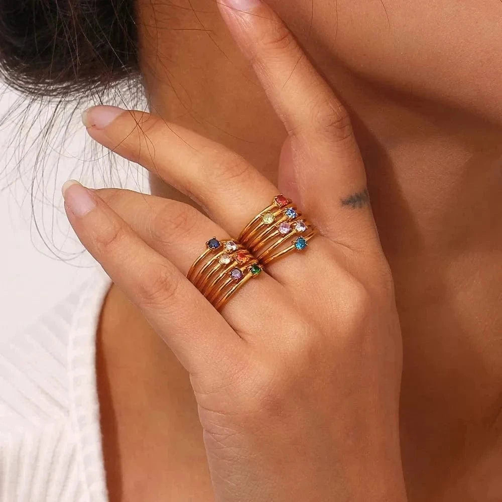 Close-up of a hand wearing multiple gold rings with colorful gemstones.